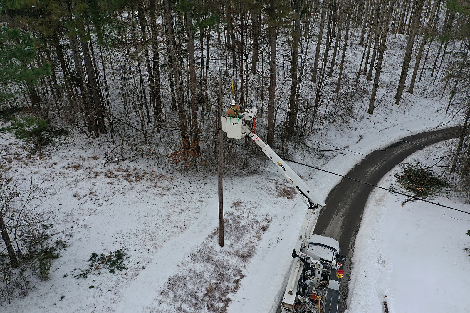 A BEA lineman working from a bucket truck at a power pole in snow-covered woods beside a country road
