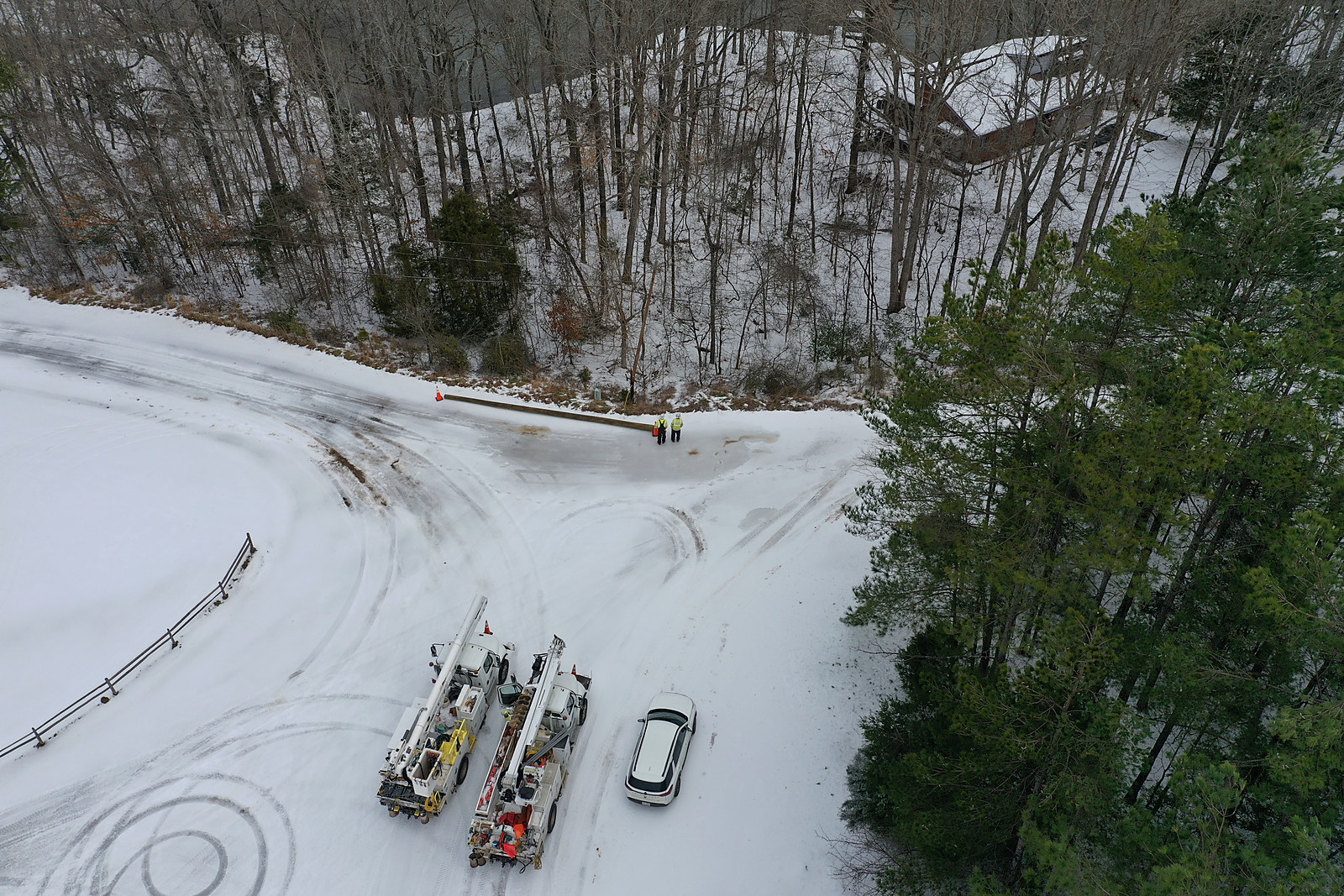 BEA trucks and crew members working on a power line along a snow-covered road, seen from above
