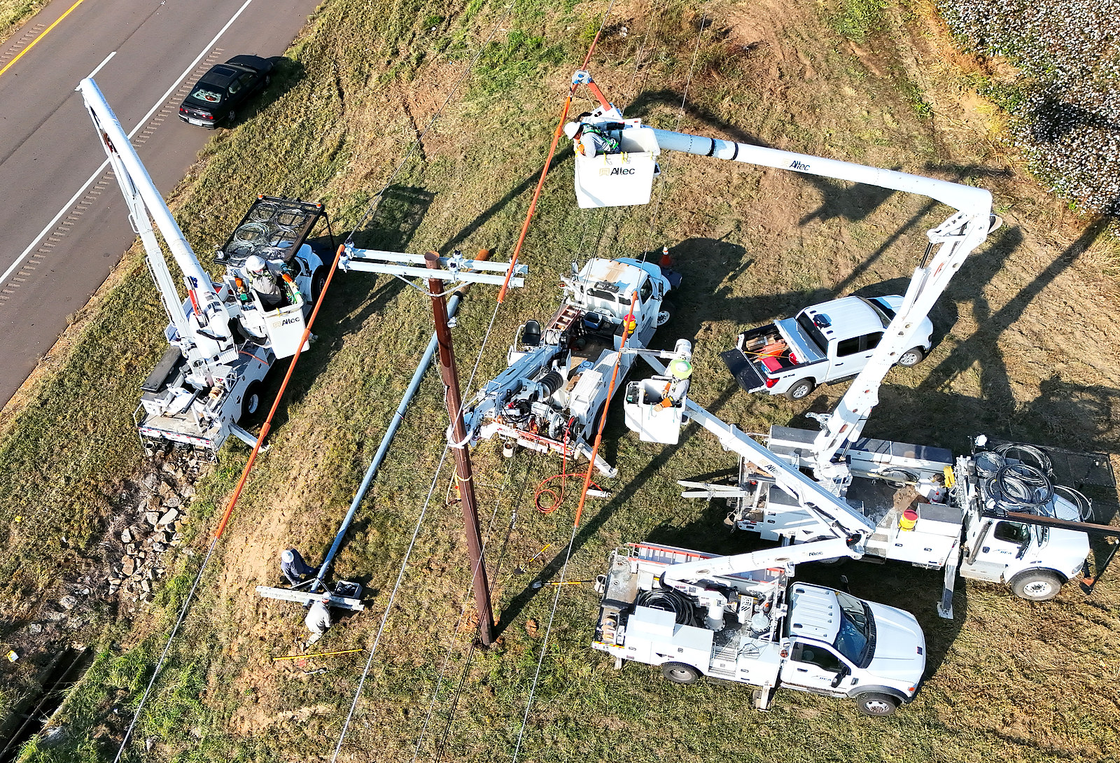 Bucket trucks and a digger derrick gathered around a power pole during a pole replacement beside a highway