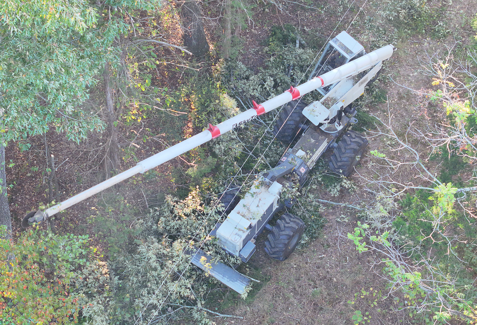 A boom mower reaching into the treeline to clear limbs away from power lines