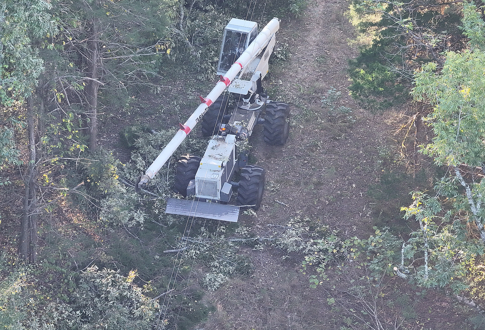 A boom mower working along a cleared power line right of way cut through the woods